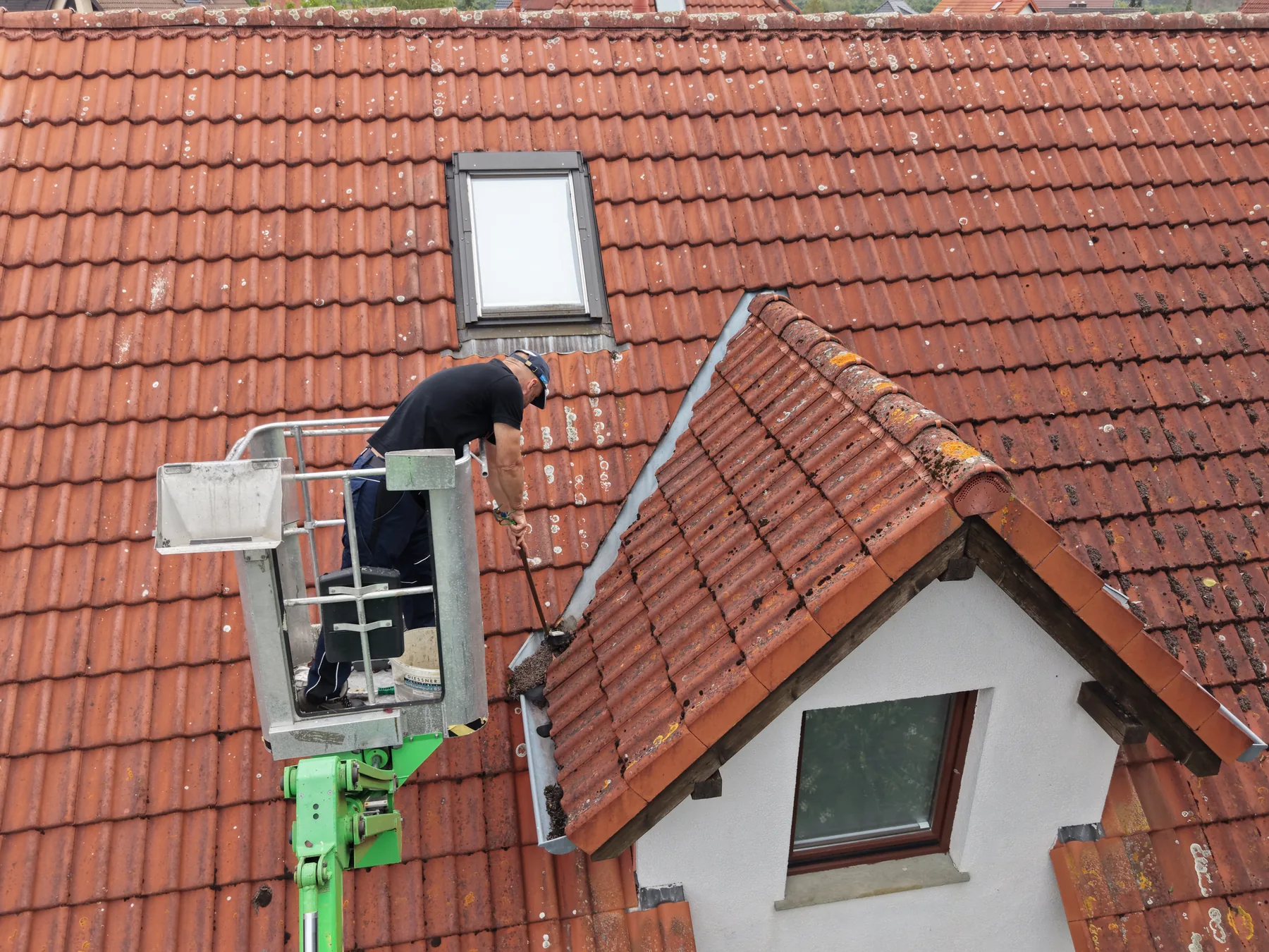 Reinigung der Dachkehle und Dachrinne neben einer Gaube mit einem Handwerkzeug